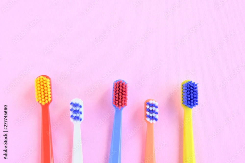 Row of Colorful toothbrushes with selective focus on blurred pink background. Dental tools for daily teeth protection. Multicolored plastic toothbrush with bright bristles with soft focus. Oral hygien Row of Colorful toothbrushes with selective focus on blurred pink background. Dental tools for daily teeth protection. Multicolored plastic toothbrush with bright bristles with soft focus. Oral hygien