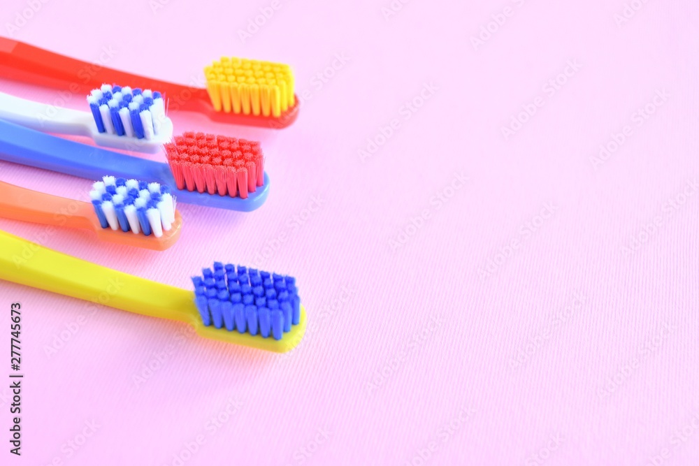 Row of Colorful toothbrushes with selective focus on blurred pink background. Dental tools for daily teeth protection. Multicolored plastic toothbrush with bright bristles with soft focus. Oral hygien Row of Colorful toothbrushes with selective focus on blurred pink background. Dental tools for daily teeth protection. Multicolored plastic toothbrush with bright bristles with soft focus. Oral hygien