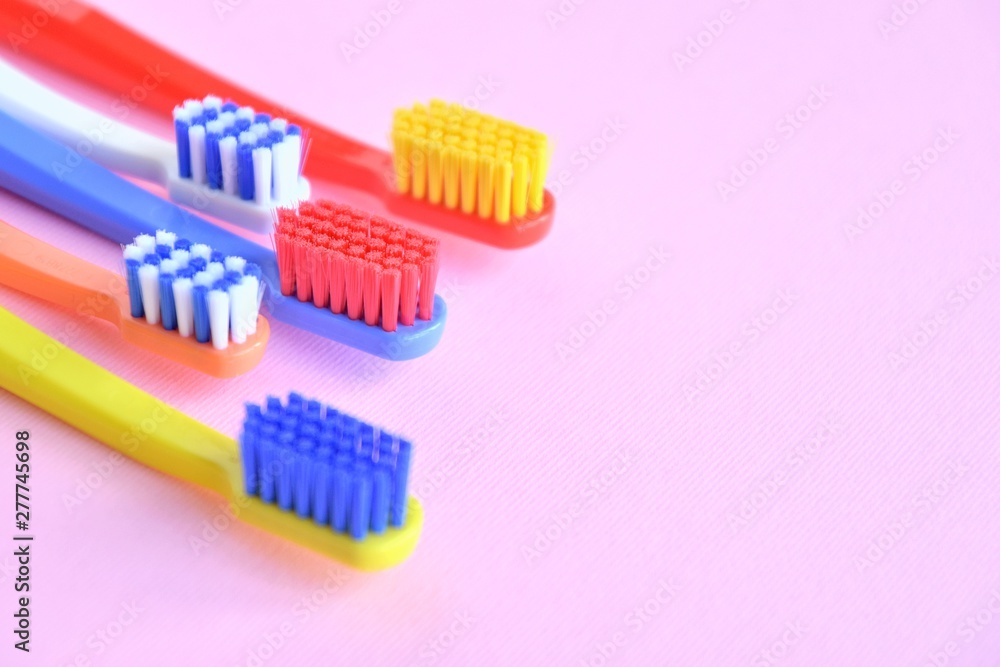 Row of Colorful toothbrushes with selective focus on blurred pink background. Dental tools for daily teeth protection. Multicolored plastic toothbrush with bright bristles with soft focus. Oral hygien Row of Colorful toothbrushes with selective focus on blurred pink background. Dental tools for daily teeth protection. Multicolored plastic toothbrush with bright bristles with soft focus. Oral hygien