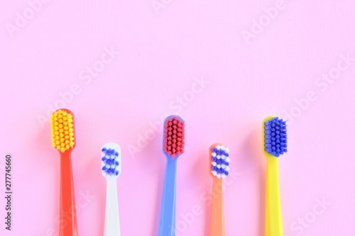 Row of Colorful toothbrushes with selective focus on blurred pink background. Dental tools for daily teeth protection. Multicolored plastic toothbrush with bright bristles with soft focus. Oral hygien