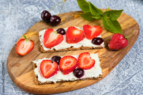 loaves with cheese, strawberries and cherries on a cutting board and gray background with mint leaves