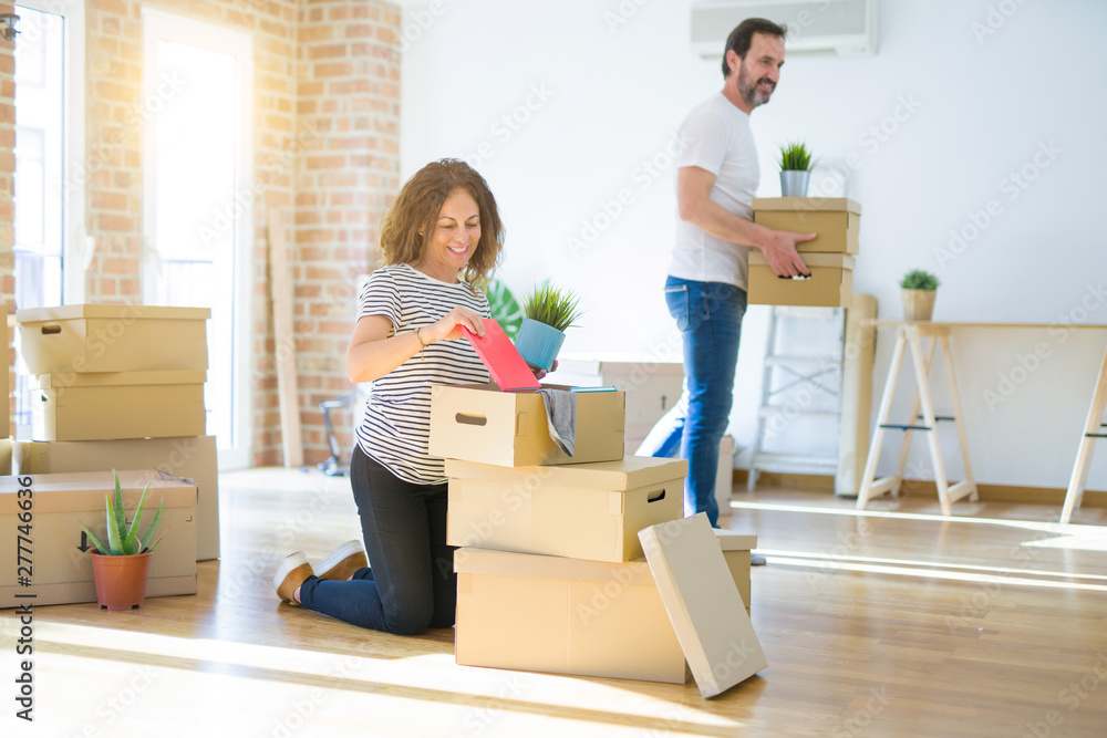 Middle age senior couple moving to a new house, smiling woman holding cardboard boxes and packaging Middle age senior couple moving to a new house, smiling woman holding cardboard boxes and packaging