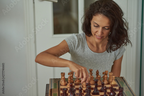  Latin brunette woman thinks of a chess move on a handmade inlay board with pieces made of olive wood in the city of Granada, in Andalusia.