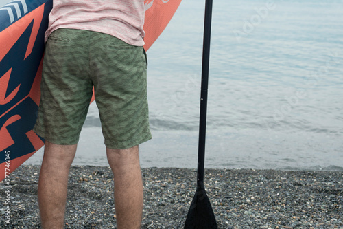 Backside section of young man with paddle board and paddle about to enter sea