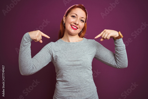 Beautiful redhead woman wearing grey t-shirt and diadem over isolated purple background looking confident with smile on face, pointing oneself with fingers proud and happy.
