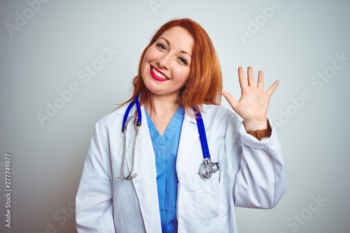 Young redhead doctor woman using stethoscope over white isolated background Waiving saying hello happy and smiling  friendly welcome gesture