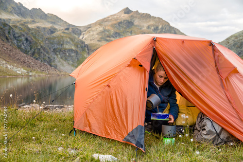 Spronser Lakes Hike, South Tyrol, Italy: A woman preparing instant food from inside her tent at the shore of the 
