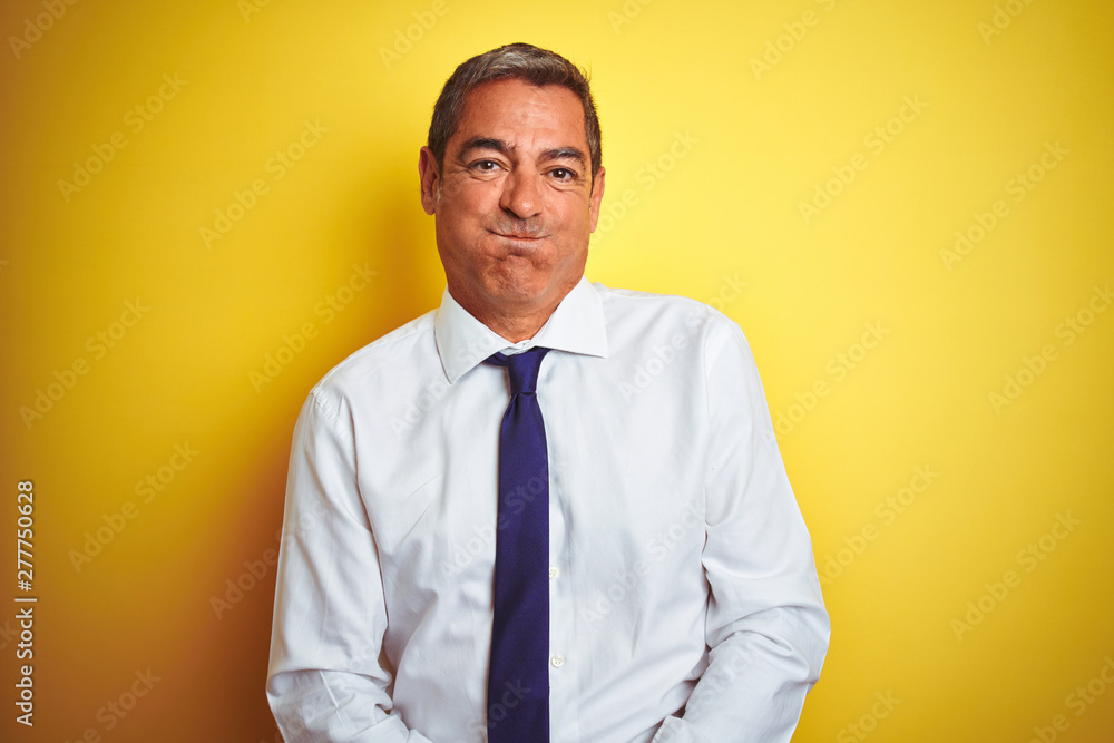 Handsome middle age businessman standing over isolated yellow background puffing cheeks with funny face. Mouth inflated with air, crazy expression. Handsome middle age businessman standing over isolated yellow background puffing cheeks with funny face. Mouth inflated with air, crazy expression.