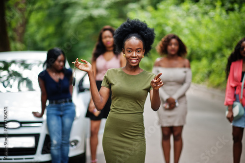 Group of five happy african american girls posed against car, one of them show keys.