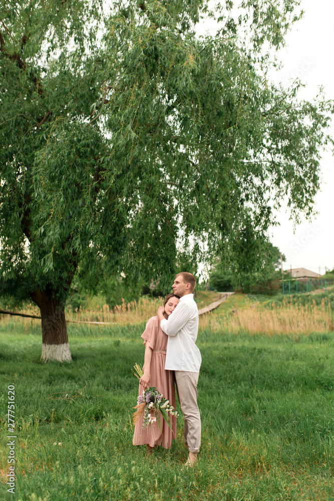 Young loving couple hugging and dancing on the green grass on the lawn. Beautiful and happy woman and man gently touch each other. Beautiful couple in love. girl in the dress and the guy in the shirt