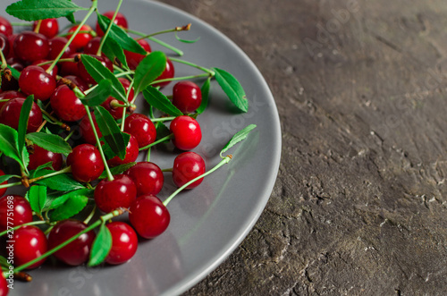 Bright,red, ripe cherry berry in a gray saucer on an old concrete, rustic background.