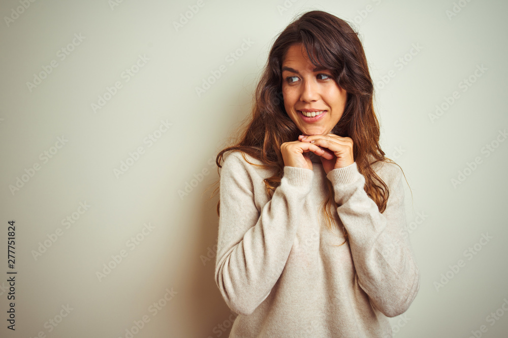 Young beautiful woman wearing winter sweater standing over white isolated background laughing nervous and excited with hands on chin looking to the side Young beautiful woman wearing winter sweater standing over white isolated background laughing nervous and excited with hands on chin looking to the side
