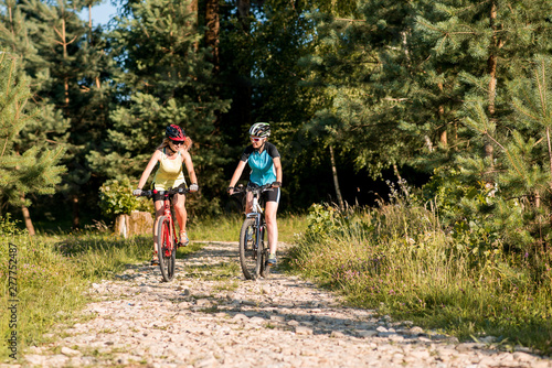 Two women friends riding bikes offroad at the forest