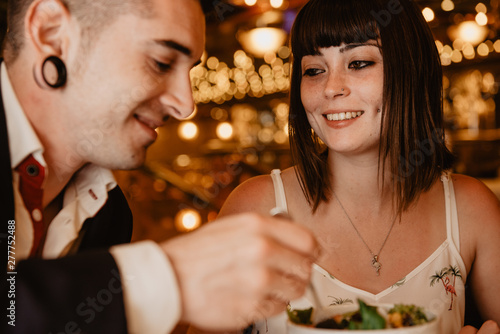 Cheerful young man and woman eating tasty fresh salad while sitting at table on blurred background of luxury restaurant during romantic dinner photo