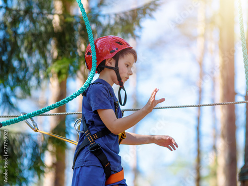 Boy in helmet is doing activity in adventure rope park with all climbing equipment.