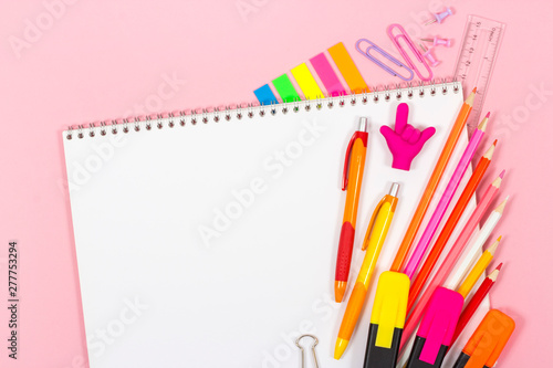 Notebook with various stationery. On a pink background.