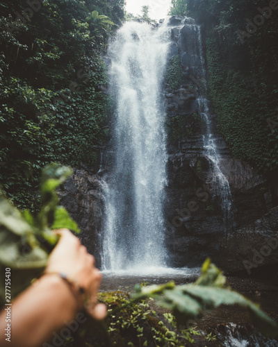 Man's hand discovering waterfall on in tropical woods photo
