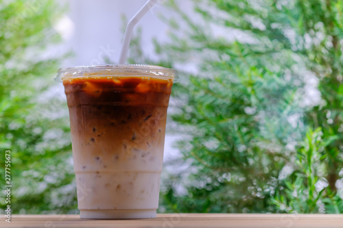Close up of take away plastic cup of iced coffee latte on wooden table with green nature as background