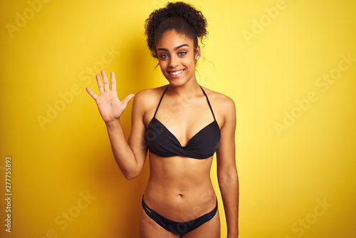 African american woman on vacation wearing bikini standing over isolated yellow background showing and pointing up with fingers number five while smiling confident and happy.