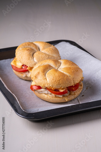 Two homemade burger Vienna Kaiser bread bun bread roll with chicken meat tomato mustard mayonnaise on baking tray sheet parchment paper white background