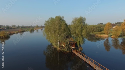 Picturesque mystical fisherman hut cabin with a bridge on a lonely fairy island of love in a beautiful lake sunny landscape in Solotvin village, Ukraine. Aerial survey, flight of drone  photo