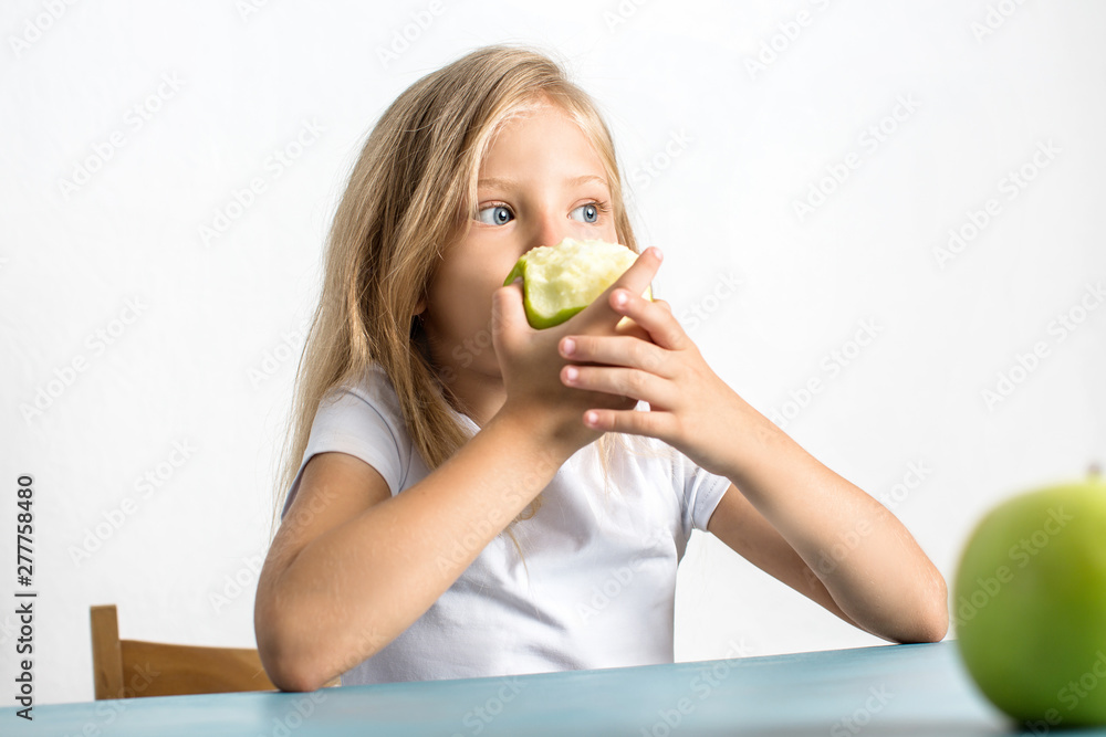Beautiful blond girl eating a green apple sitting at the table Beautiful blond girl eating a green apple sitting at the table