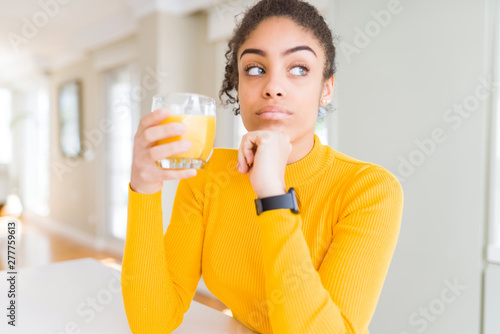 Young african american woman drinking a glass of fresh orange juice serious face thinking about question, very confused idea