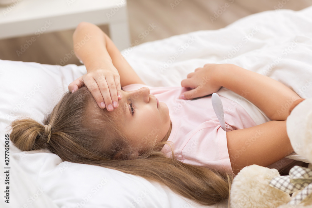 Sick little child girl lying in bed with thermometer. Cold flu season