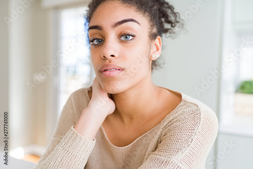 Fotografi Beautiful young african american woman with blue eyes relaxing at home, with con