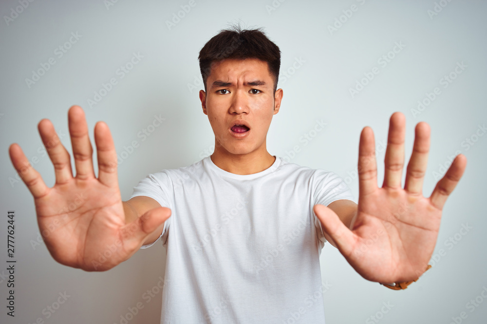 Young asian chinese man wearing t-shirt standing over isolated white background doing stop gesture with hands palms, angry and frustration expression Young asian chinese man wearing t-shirt standing over isolated white background doing stop gesture with hands palms, angry and frustration expression