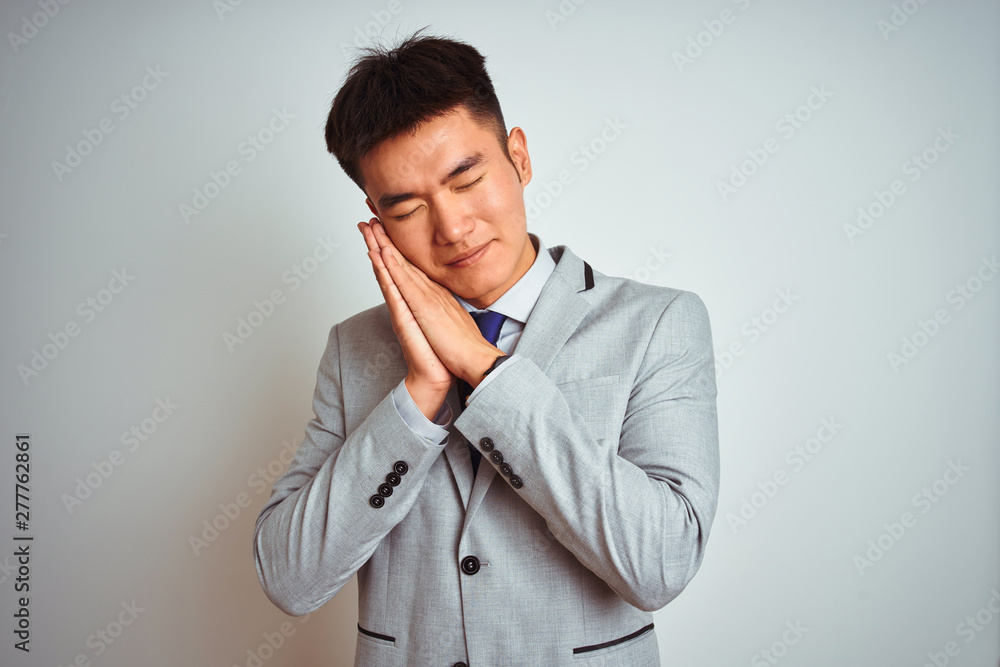 Asian chinese businessman wearing suit and tie standing over isolated yellow background sleeping tired dreaming and posing with hands together while smiling with closed eyes. Asian chinese businessman wearing suit and tie standing over isolated yellow background sleeping tired dreaming and posing with hands together while smiling with closed eyes.