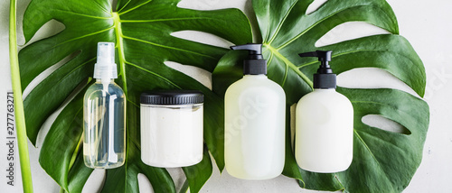 Cosmetic set of blank label bottles for mockup packaging of skincare product cream  serum  oil  shampoo  conditioner  perfume on grey background with green leaves. Natural beauty product concept.