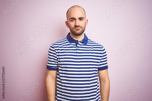 Young bald man with beard wearing casual striped blue t-shirt over pink isolated background Relaxed with serious expression on face. Simple and natural looking at the camera.