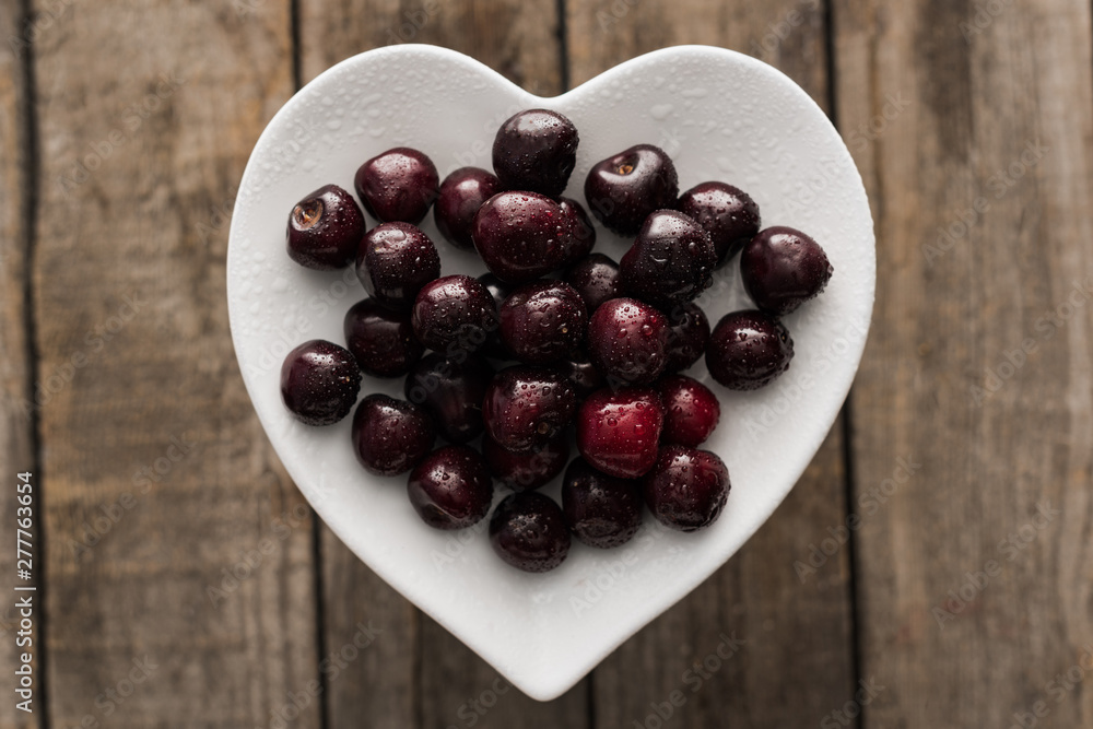 top view of red, fresh, whole and ripe cherries covered with droplets on plate on wooden surface top view of red, fresh, whole and ripe cherries covered with droplets on plate on wooden surface