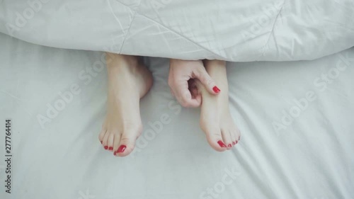 Female legs in bed view from above, white bedding, scratching photo