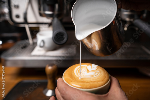 From above crop hands of professional employee preparing cappuccino with pattern on top in coffee shop photo
