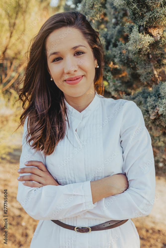 Positive young female in stylish blouse smiling and keeping arms crossed  while standing in park on sunny day Stock Photo | Adobe Stock