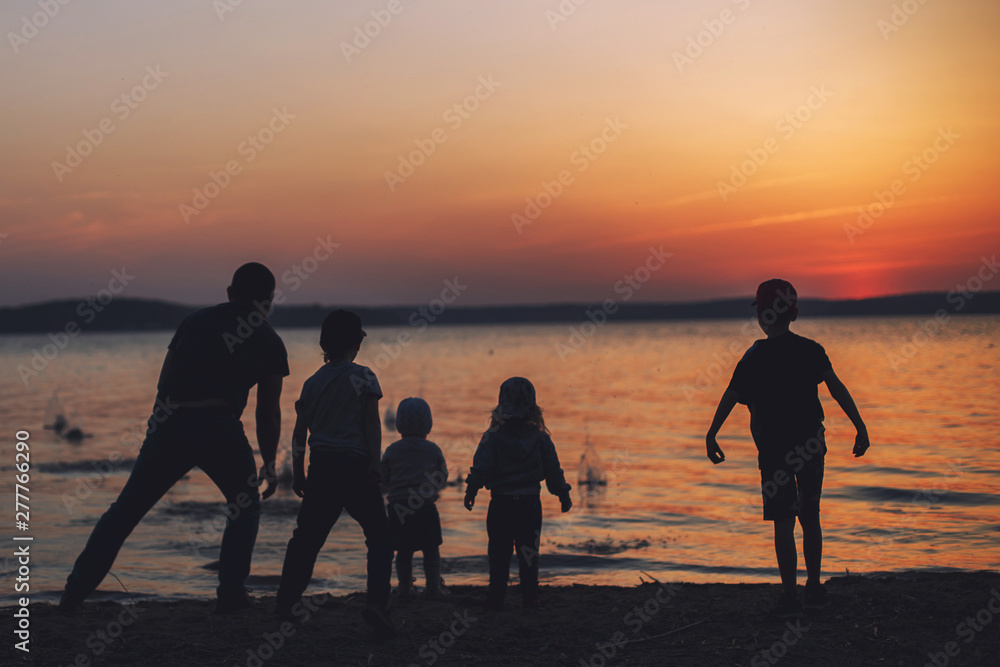 people at sunset throwing stones into the water. dad with children