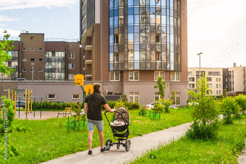 Father with son in a stroller walk along the sidewalk in the vicinity of the city. A child in a baby carriage and a man in the background of nature. Family holiday on a vacations.