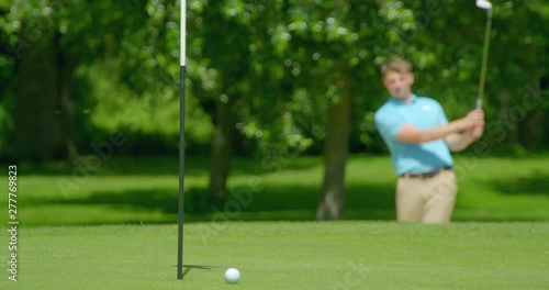 Rack Focus shot of golfer chipping out of a sand trap / bunker onto the green.