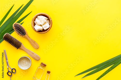 Cosmetics for hair care with jojoba, argan or coconut oil in bottle, comb, scissors on yellow background top view mockup