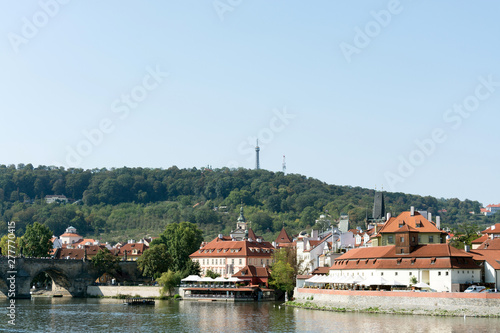 Waterfront panorama of Vltava river, colorful rooftops of New Town and Petrin lookout tower on a bright summer day, in Prague, Czech Republic