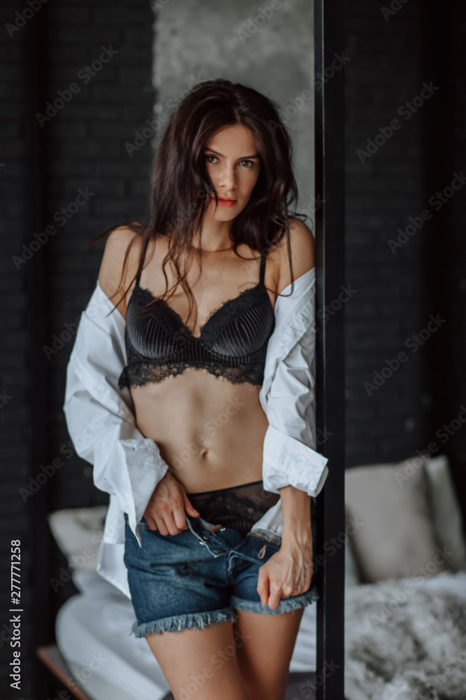 Sexy brunette girl in black underwear takes off her clothes next to the  bed. dark background foto de Stock | Adobe Stock