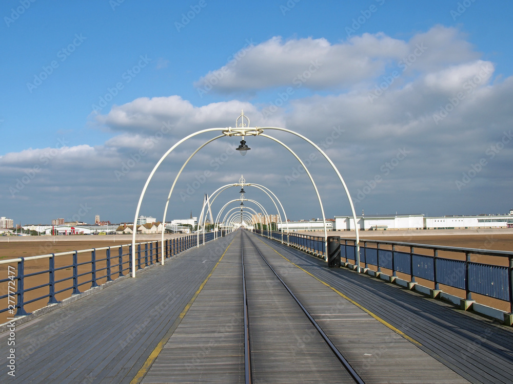 Obraz premium a panoramic view along the pier in southport merseyside with the beach at low tide on a bright summer day with the waterfront buildings of the town against a blue cloudy sky