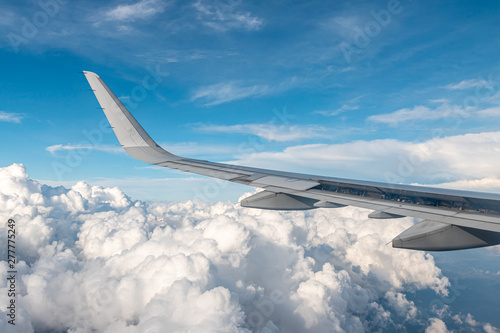 Large commercial airplane wing curving. The blue skyline view above the clouds from air plane window.