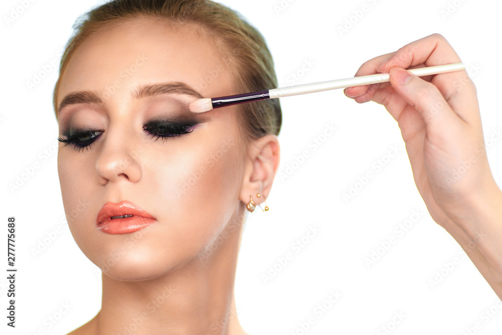 Makeup artist paints the eyes of a woman client shadows on a brush