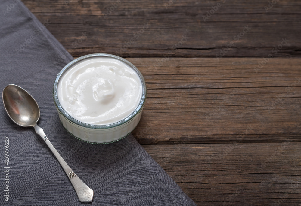 White yogurt in glass bowl on old wooden desk with spoon on left side. White yogurt in glass bowl on old wooden desk with spoon on left side.