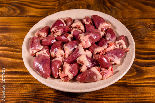 Ceramic plate with raw chicken hearts on wooden table