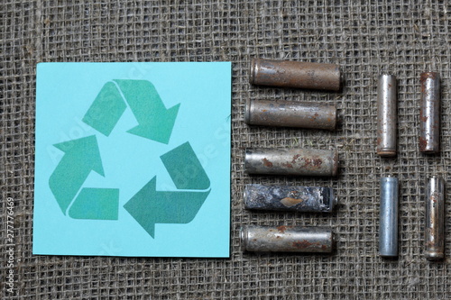 Spent batteries lie on a rough linen background. Covered with corrosion. Nearby is the recycling sign of the Möbius loop. Recycling and environmental protection.