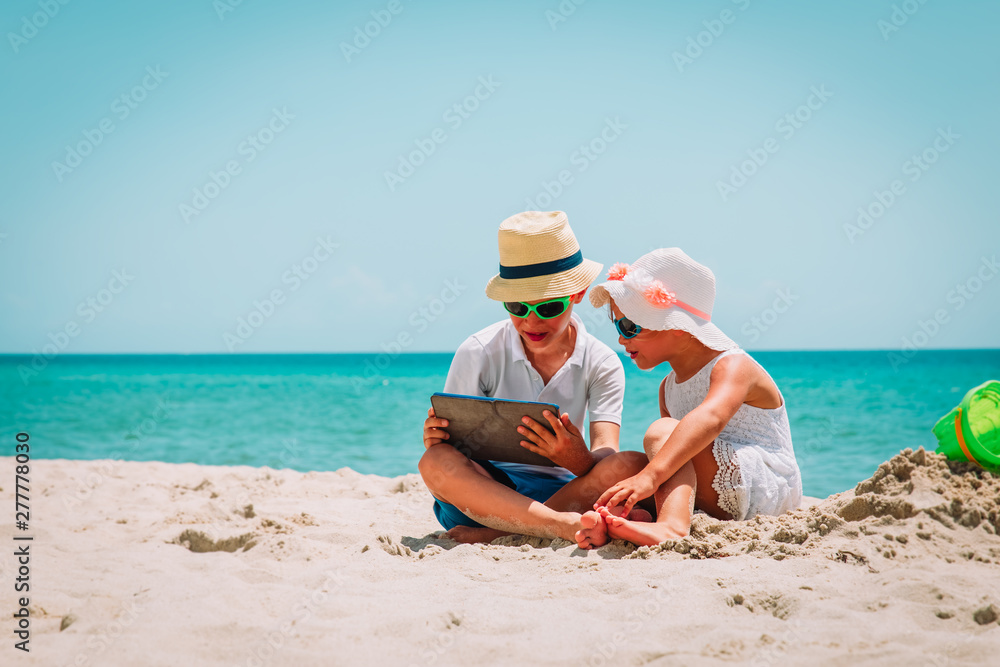 happy cute boy and girl looking at touch pad at beach happy cute boy and girl looking at touch pad at beach